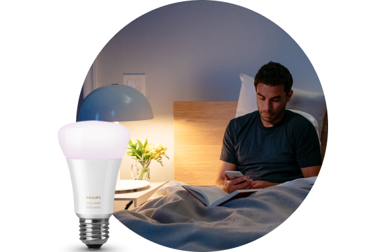 Image with a smart light bulb in the forefront with a lit nightstand lamp in the background